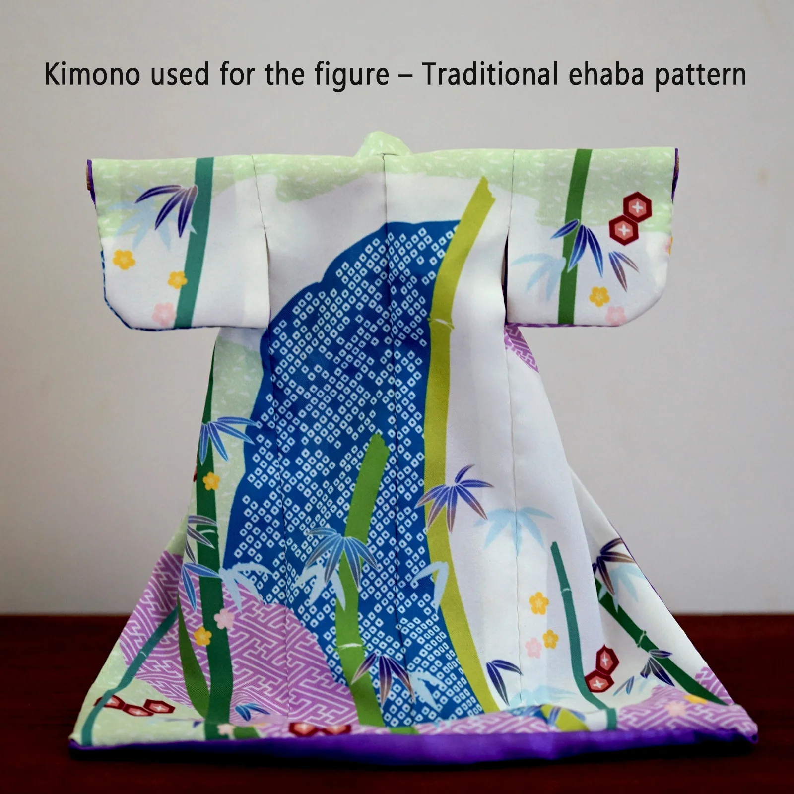 Doll-size kimono with pale green fabric, bamboo and small flower patterns, and a blue kanoko-shibori-inspired motif at the center